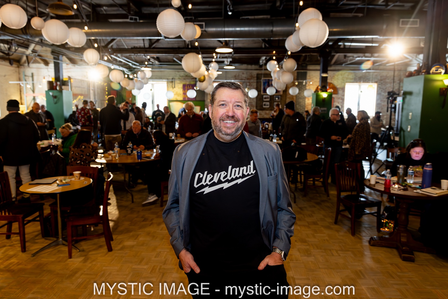 Jim Kukral, the marketing and sales author who personally reviews every Review Report, smiling in a busy workspace full of people at tables. Photograph credit Mystic Image.